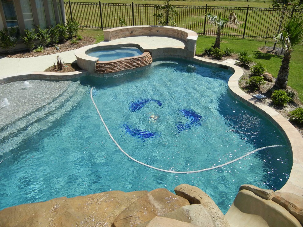 Modelo de piscina con tobogán marinera grande a medida en patio trasero con suelo de hormigón estampado