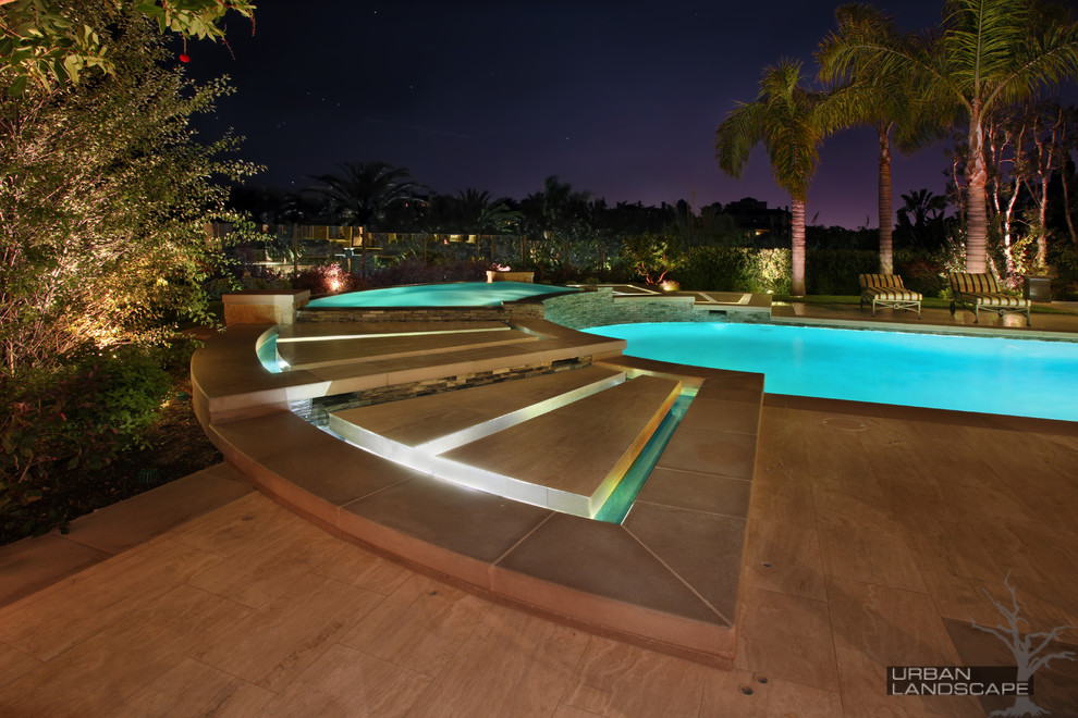 This is an example of a large classic back custom shaped infinity swimming pool in Orange County with a water feature and natural stone paving.