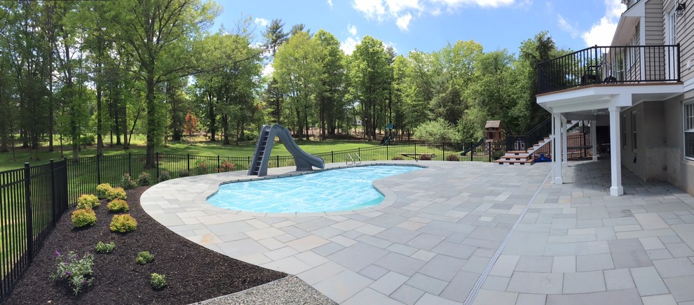 Ejemplo de piscina con tobogán alargada tradicional de tamaño medio tipo riñón en patio trasero con suelo de baldosas