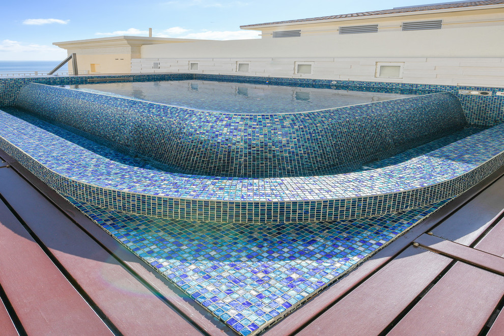 Immagine di una piccola piscina a sfioro infinito mediterranea personalizzata sul tetto con una vasca idromassaggio e pavimentazioni in pietra naturale