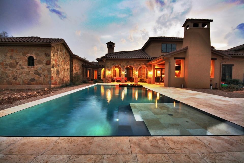 Aménagement d'une grande piscine à débordement et arrière méditerranéenne rectangle avec des pavés en pierre naturelle et un bain bouillonnant.