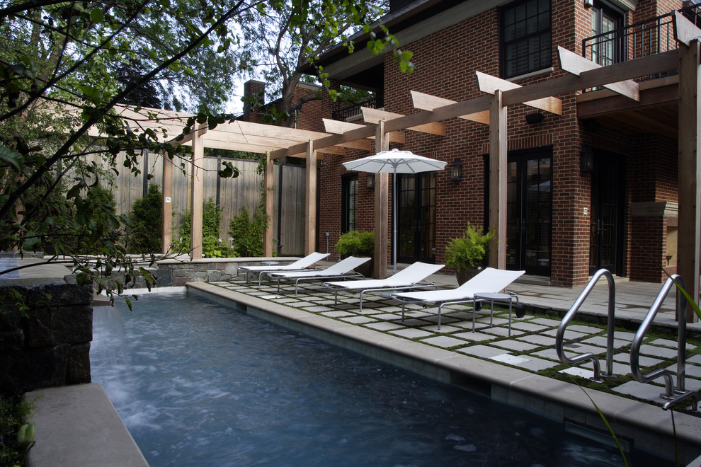 Photo of a medium sized contemporary back rectangular swimming pool in Chicago with natural stone paving and a water feature.