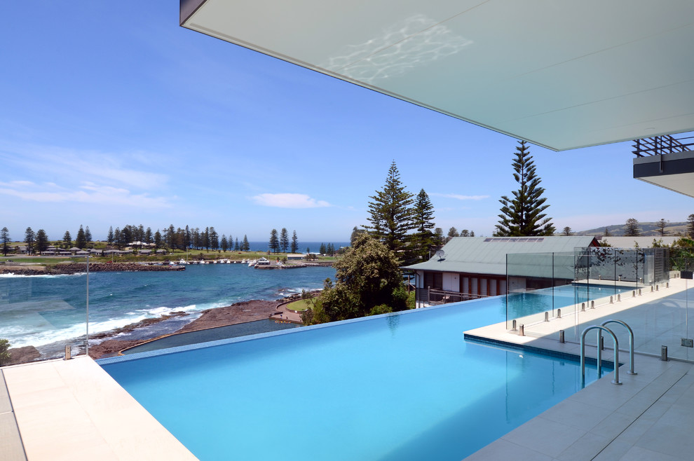 This is an example of a medium sized modern back l-shaped infinity swimming pool in Wollongong with a pool house and tiled flooring.