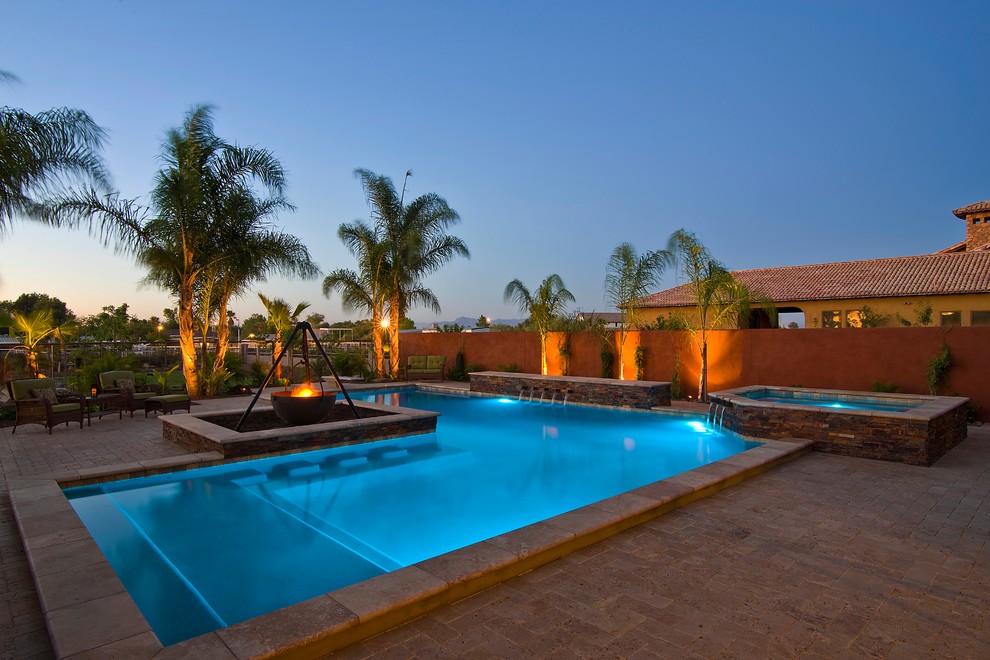 Modelo de piscina con fuente alargada tradicional grande en forma de L en patio trasero con adoquines de hormigón
