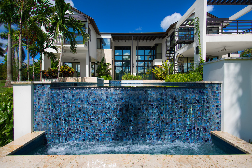 Esempio di una grande piscina a sfioro infinito design rettangolare dietro casa con fontane e pavimentazioni in pietra naturale