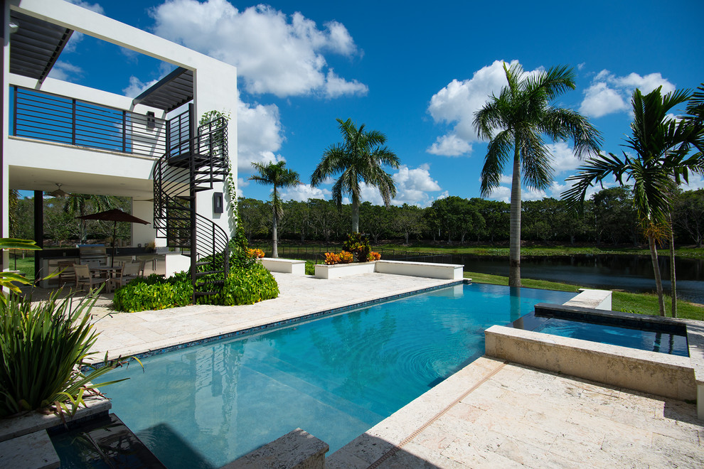 Ejemplo de piscina con fuente infinita actual grande rectangular en patio trasero con adoquines de piedra natural