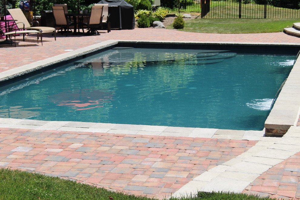 Large classic back rectangular natural swimming pool in DC Metro with a water feature and brick paving.