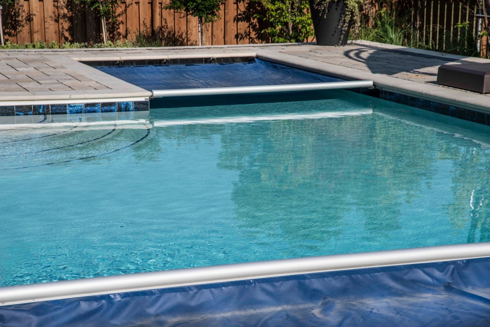 Diseño de piscina alargada tradicional de tamaño medio en forma de L en patio trasero con adoquines de hormigón