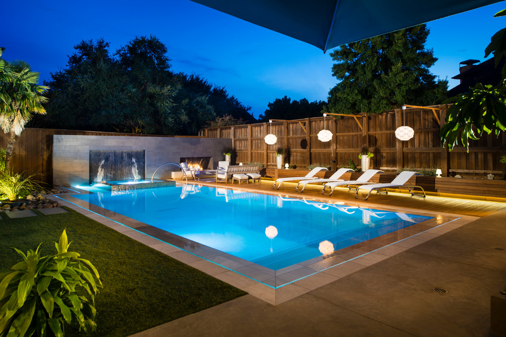 Esempio di una grande piscina monocorsia design rettangolare dietro casa con fontane e lastre di cemento