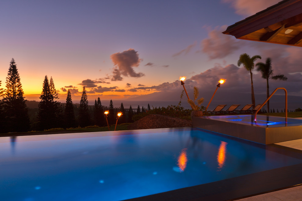 Esempio di una grande piscina a sfioro infinito tropicale rettangolare dietro casa con una vasca idromassaggio e lastre di cemento