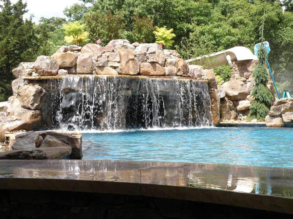 This is an example of a large classic back custom shaped swimming pool in Kansas City with a water feature.