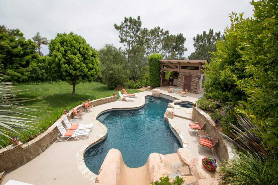 This is an example of a large traditional back custom shaped swimming pool in San Diego with a pool house and concrete paving.