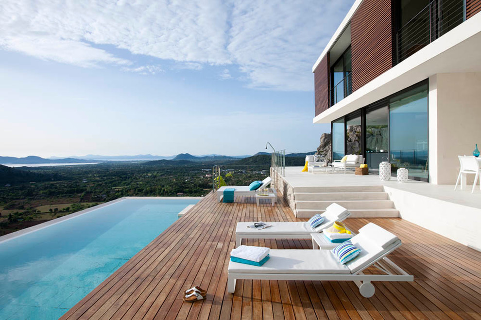 Exemple d'une grande piscine à débordement et arrière tendance rectangle avec une terrasse en bois.