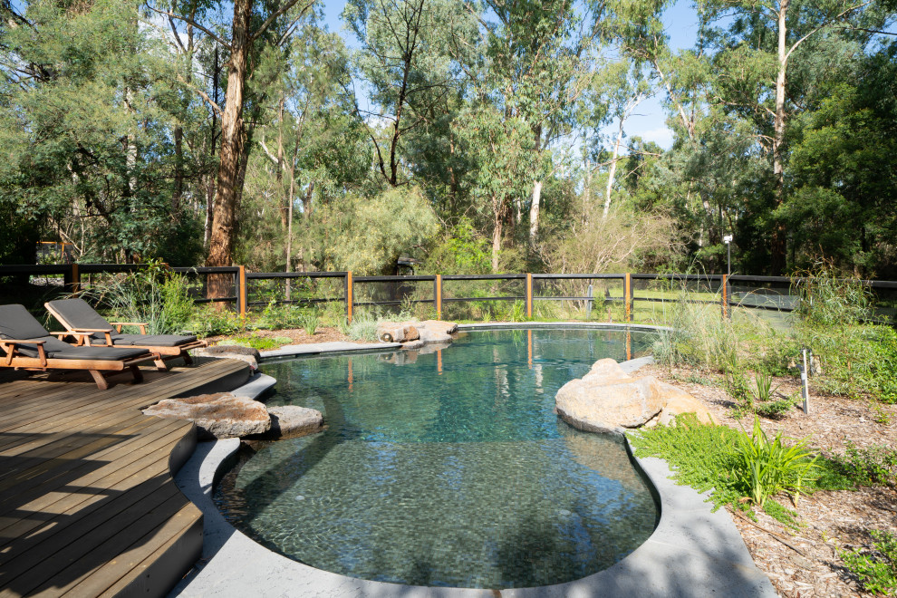 This is an example of a large back custom shaped natural swimming pool in Melbourne with a pool house and natural stone paving.