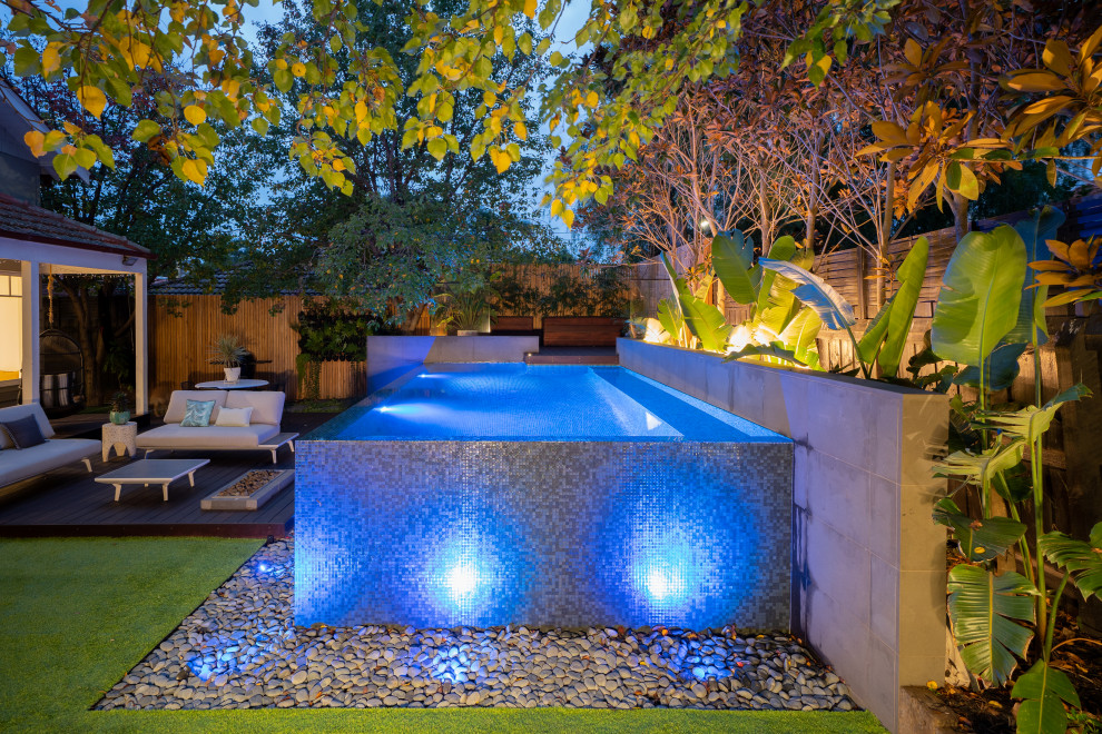 Diseño de piscina infinita tropical pequeña rectangular en patio trasero con paisajismo de piscina y suelo de baldosas