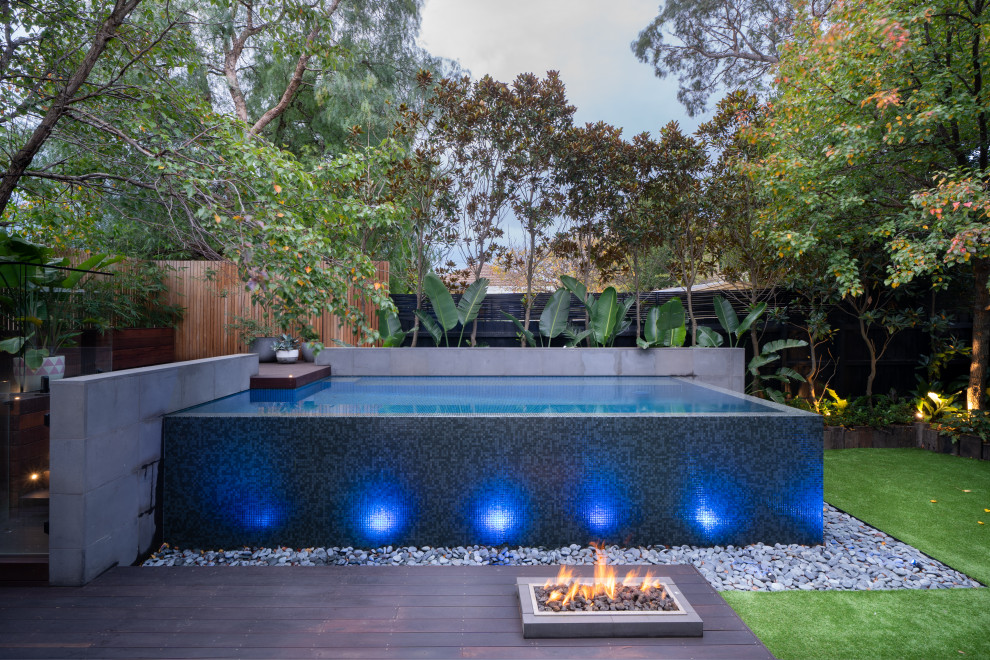 Foto de piscina infinita tropical pequeña rectangular en patio trasero con paisajismo de piscina y suelo de baldosas