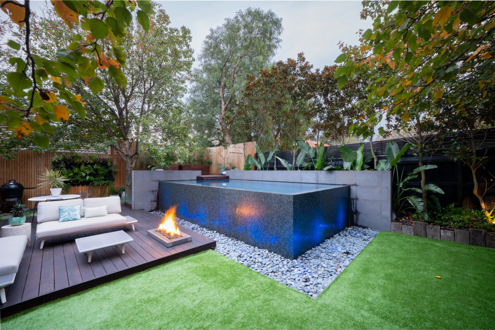 This is an example of a small world-inspired back rectangular infinity swimming pool in Melbourne with with pool landscaping and tiled flooring.