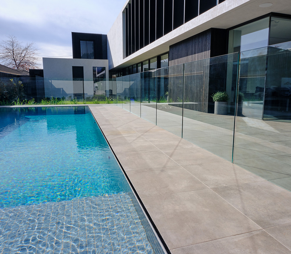 Foto de piscina alargada moderna de tamaño medio rectangular en patio trasero con paisajismo de piscina y suelo de baldosas