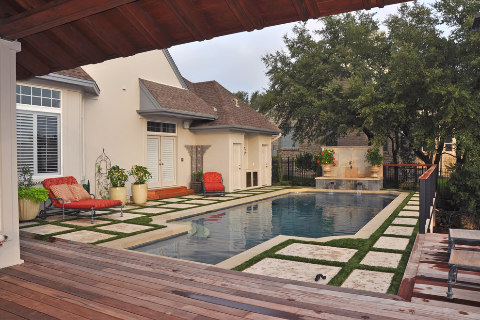 Modelo de piscina con fuente elevada clásica grande rectangular en patio trasero con adoquines de hormigón