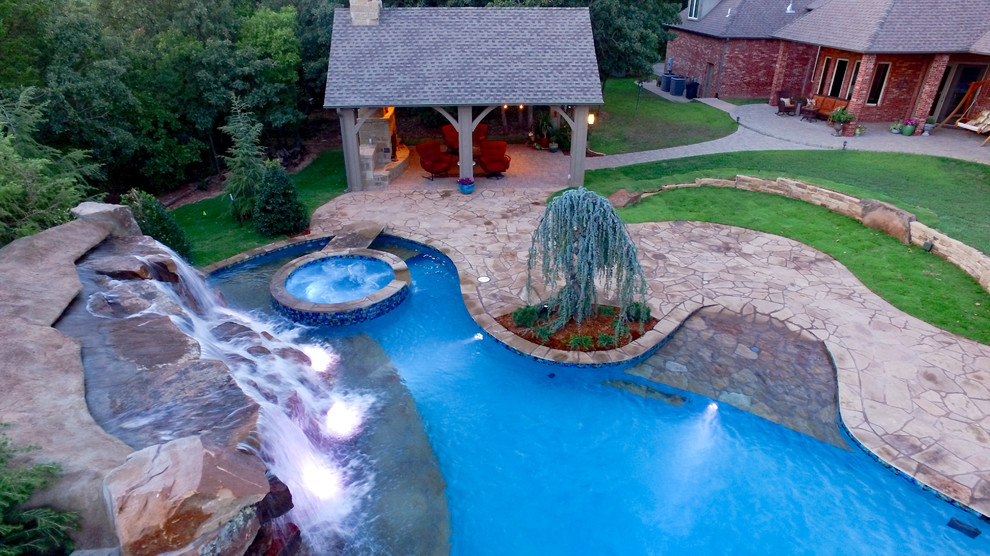 Medium sized traditional back custom shaped natural swimming pool in Oklahoma City with a water feature and natural stone paving.