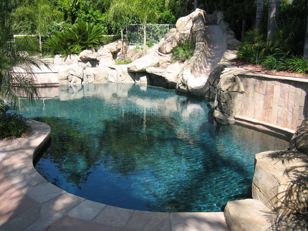 Foto på en mellanstor tropisk pool på baksidan av huset, med vattenrutschkana och naturstensplattor