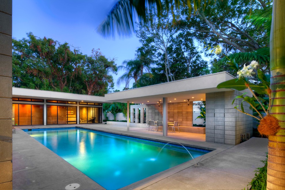 Diseño de piscina con fuente minimalista rectangular en patio con losas de hormigón