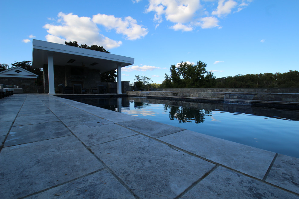 Modern inredning av en stor rektangulär baddamm på baksidan av huset, med poolhus och naturstensplattor