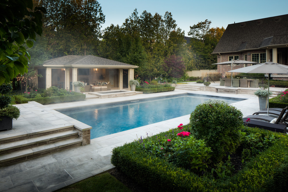 На фото: большой прямоугольный бассейн на заднем дворе в стиле неоклассика (современная классика) с домиком у бассейна и покрытием из каменной брусчатки с