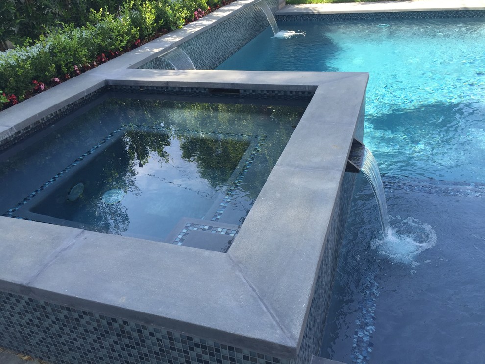 Modelo de piscina con fuente natural mediterránea de tamaño medio rectangular en patio trasero con adoquines de hormigón