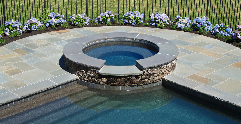 Cette image montre une grande piscine naturelle et arrière traditionnelle ronde avec un bain bouillonnant et des pavés en pierre naturelle.
