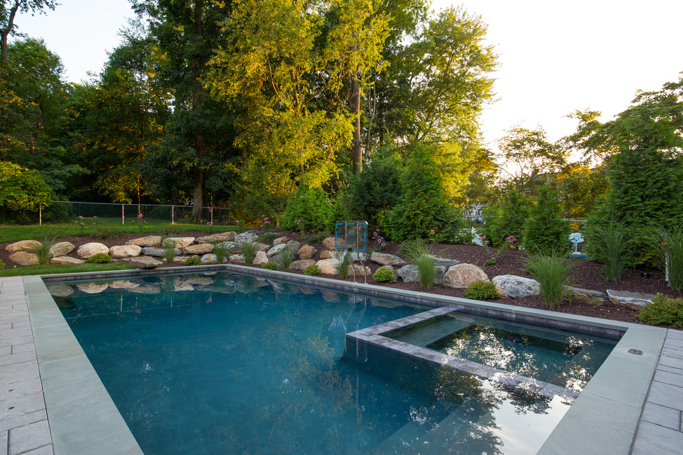 Esempio di una grande piscina monocorsia chic rettangolare dietro casa con una vasca idromassaggio e pavimentazioni in pietra naturale