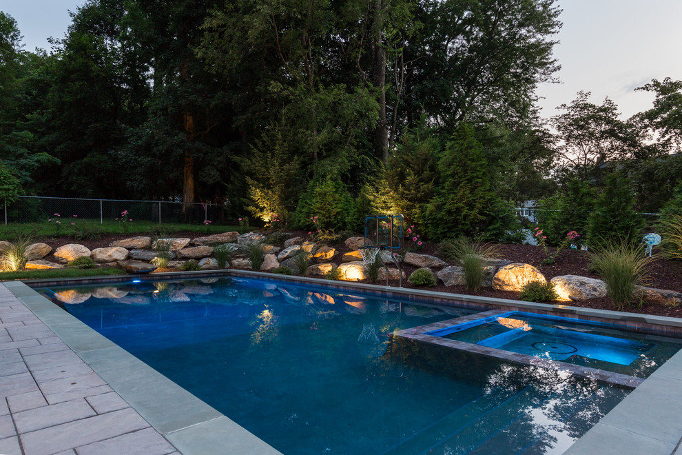 Modelo de piscinas y jacuzzis alargados clásicos grandes rectangulares en patio trasero con adoquines de piedra natural