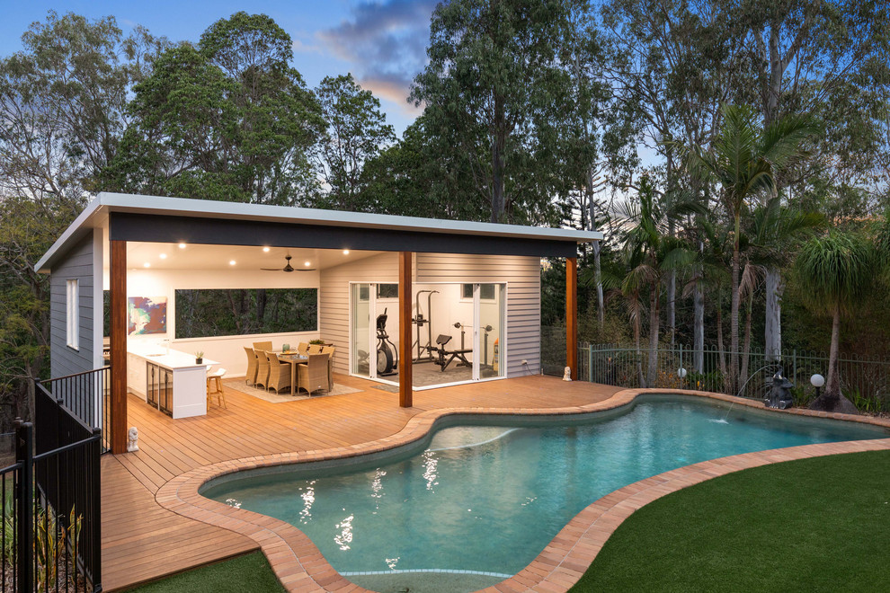 This is an example of an expansive modern back rectangular natural swimming pool in Brisbane with a pool house and decking.