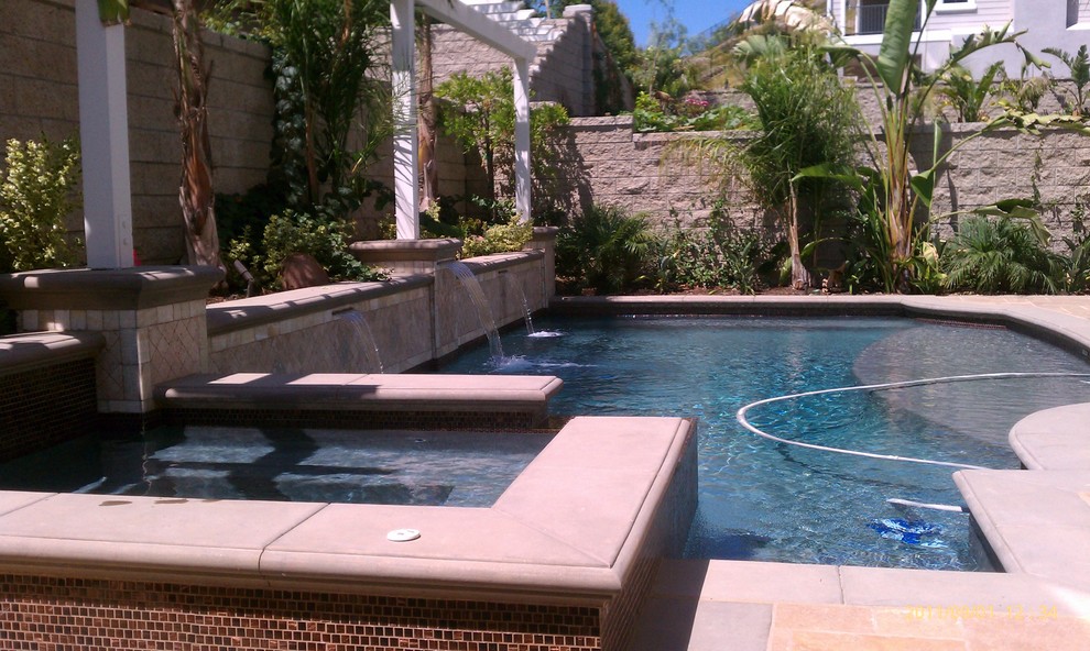 Ejemplo de piscina con fuente alargada clásica grande a medida en patio trasero con suelo de baldosas