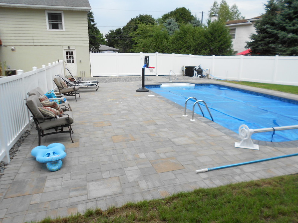 Modelo de piscina alargada tradicional grande rectangular en patio trasero con adoquines de ladrillo