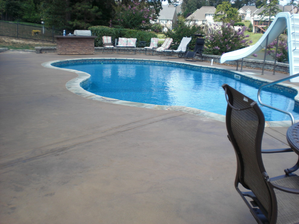 Imagen de piscina con tobogán tipo riñón en patio trasero con losas de hormigón