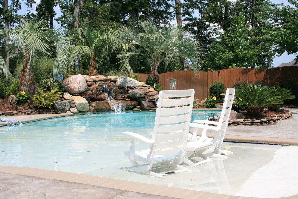 Modelo de piscina con fuente alargada tropical de tamaño medio a medida en patio trasero con adoquines de piedra natural