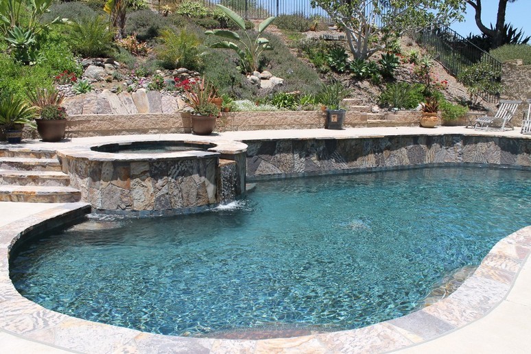 Foto på en stor pool på baksidan av huset, med spabad och marksten i betong