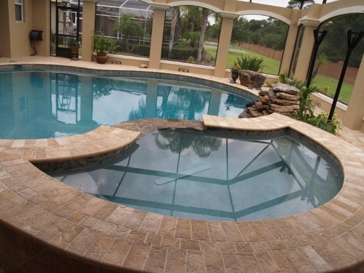 Esempio di una piscina monocorsia tropicale rettangolare di medie dimensioni e dietro casa con una vasca idromassaggio e pavimentazioni in pietra naturale