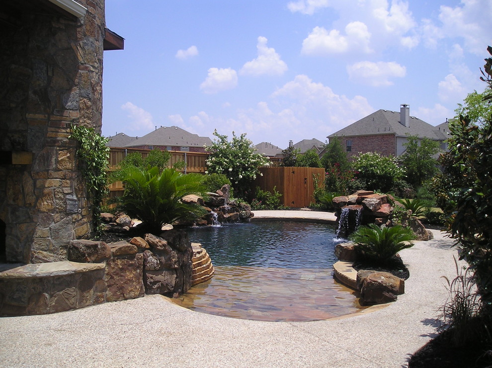 Ispirazione per una grande piscina naturale american style personalizzata dietro casa con fontane e lastre di cemento