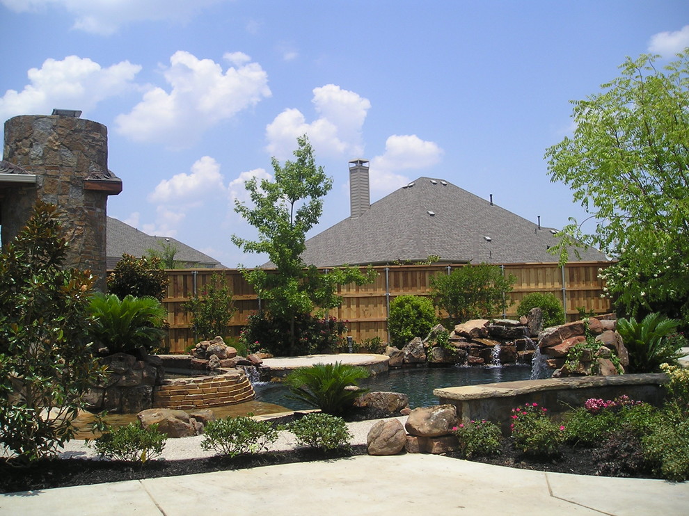 Esempio di una grande piscina naturale american style personalizzata dietro casa con fontane e lastre di cemento