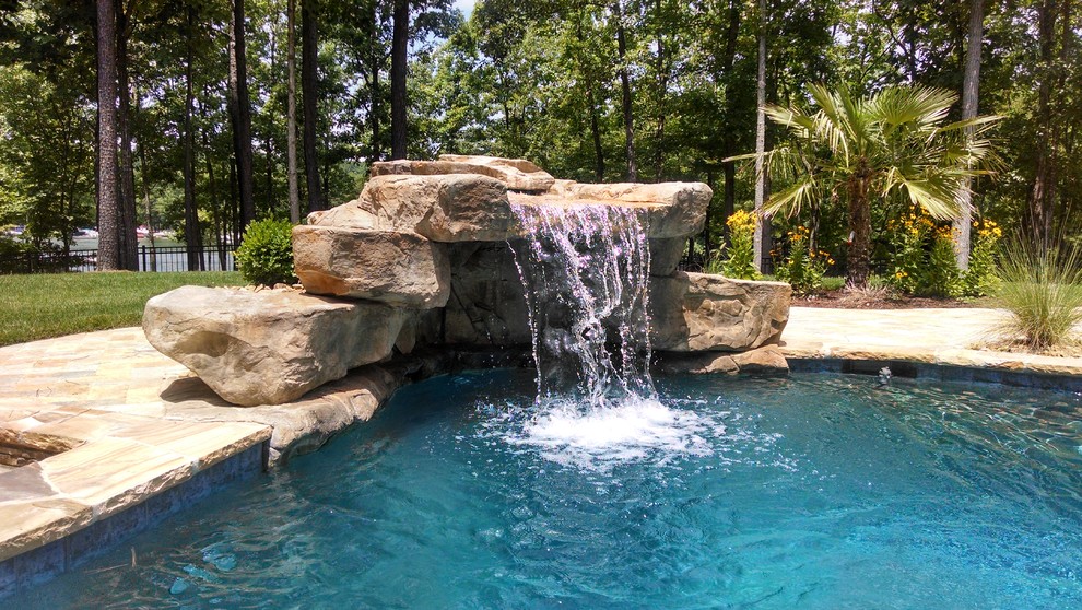 Imagen de piscina con fuente tropical grande a medida en patio trasero con adoquines de piedra natural
