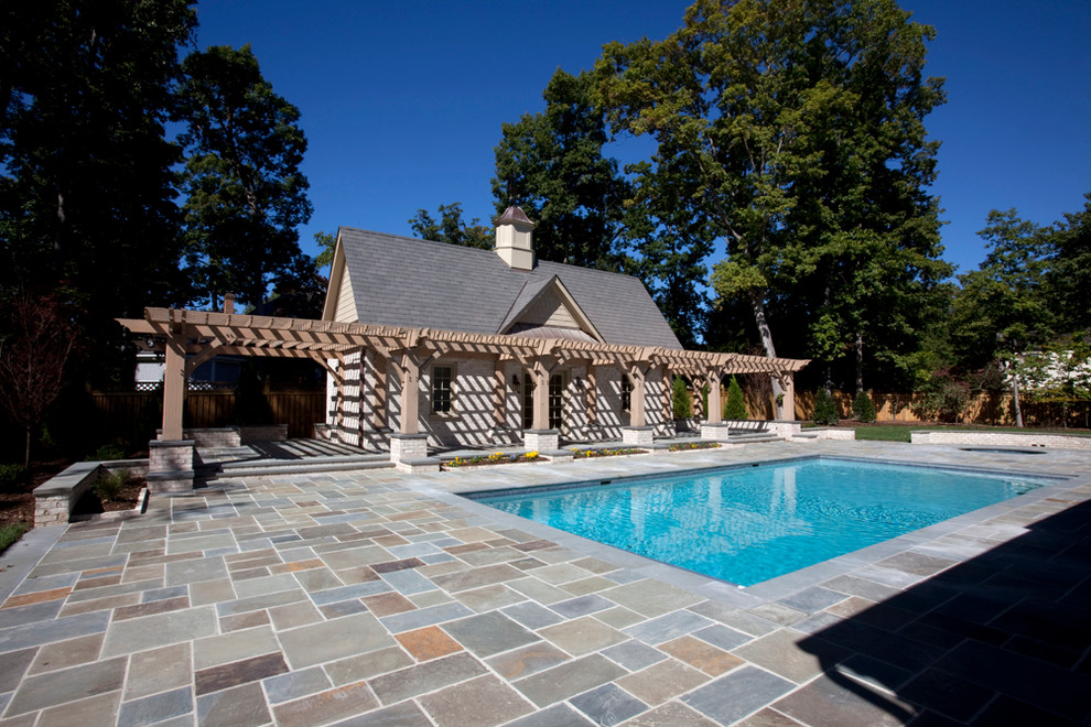 Exempel på en stor klassisk rektangulär baddamm på baksidan av huset, med poolhus och naturstensplattor
