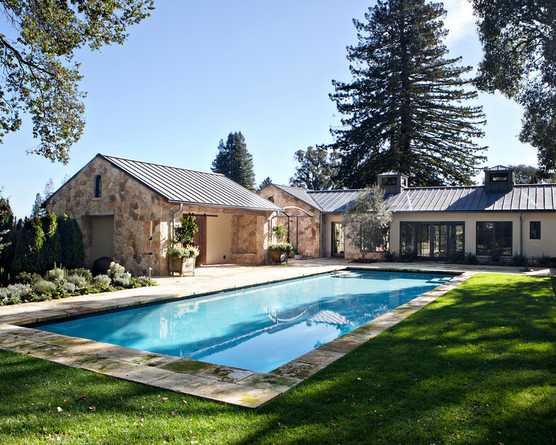 Bild på en stor lantlig rektangulär träningspool på baksidan av huset, med poolhus och naturstensplattor
