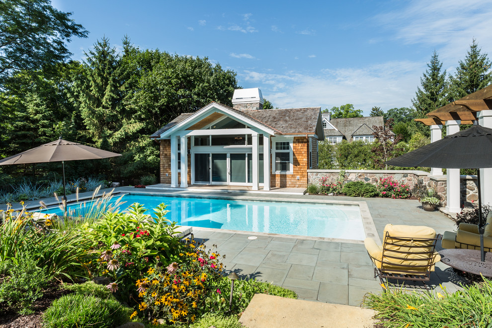 Exempel på en liten klassisk rektangulär baddamm längs med huset, med poolhus och naturstensplattor