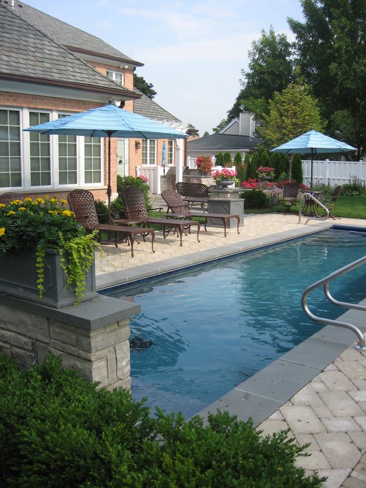 Imagen de piscina alargada tradicional rectangular en patio trasero con adoquines de piedra natural