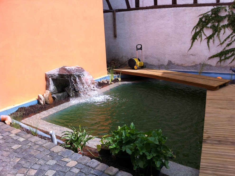Exempel på en liten medelhavsstil anpassad baddamm på baksidan av huset, med naturstensplattor