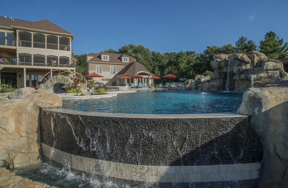 This is an example of an expansive back custom shaped infinity swimming pool in Chicago with a water feature and natural stone paving.
