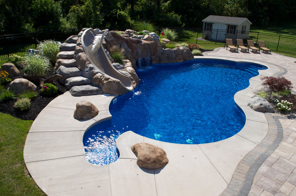 Modelo de piscina con tobogán costera grande a medida en patio trasero con suelo de hormigón estampado