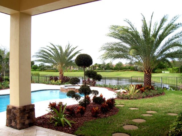 Diseño de piscina con fuente natural tropical grande a medida en patio trasero con adoquines de ladrillo